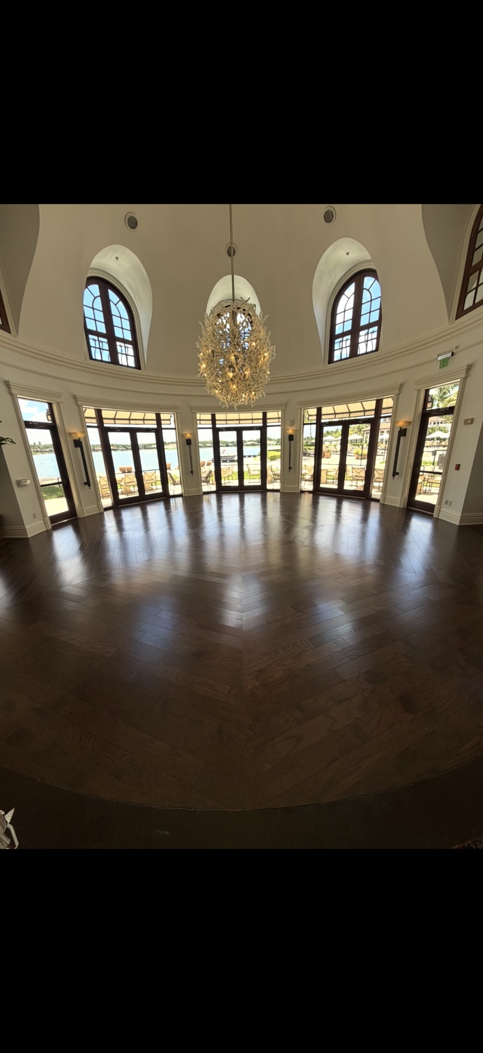 Dark hardwood flooring in a grand room with a chandelier, arched windows and waterfront views