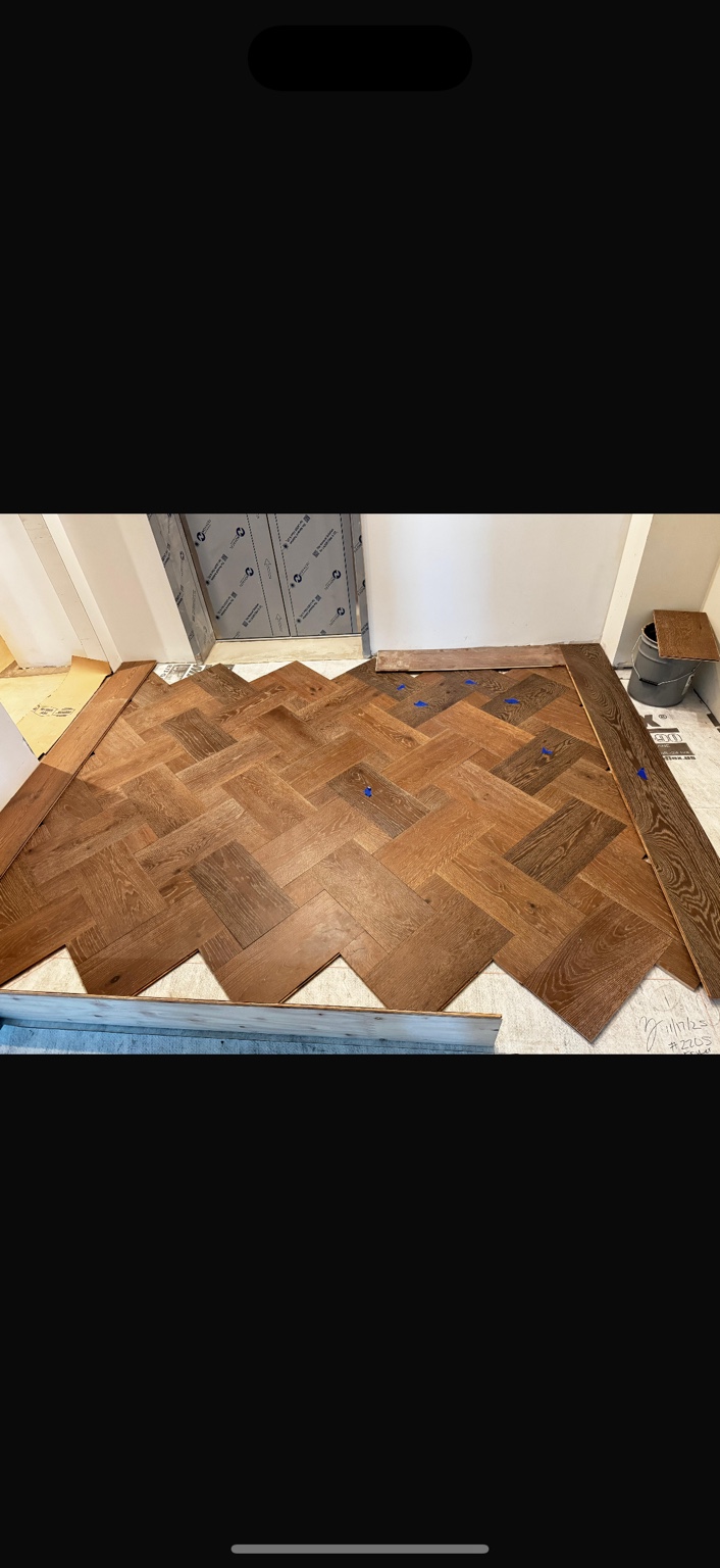 Wood herringbone flooring and border installation in progress at an elevator entry