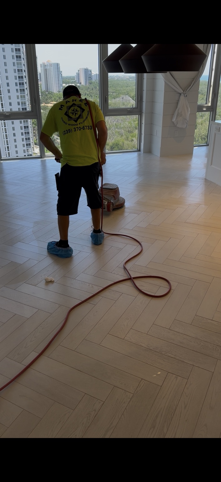 Technician buffing a light herringbone wood floor during maintenance oil treatment